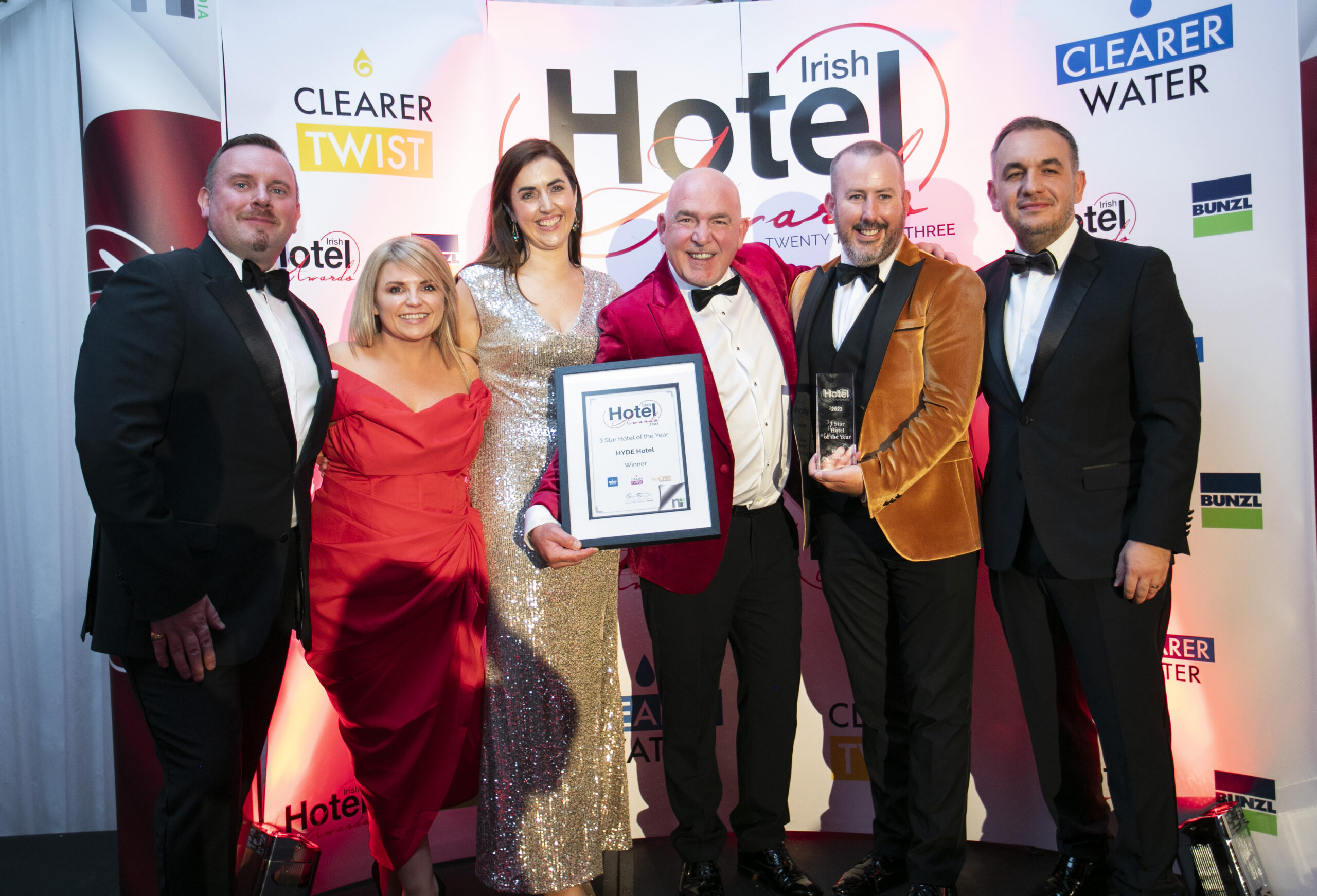 Hotel Team Celebrating an Award at the Irish Hotel Awards – A team of six, dressed in formal attire, stands on a stage holding an award at the Irish Hotel Awards. The event branding and sponsor logos are visible in the background.