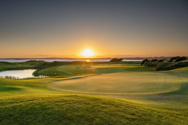 Sunset Over Galway Bay Golf Course – A breathtaking view of a golf course at sunset, with rolling green fairways leading to a golden horizon over a calm body of water.