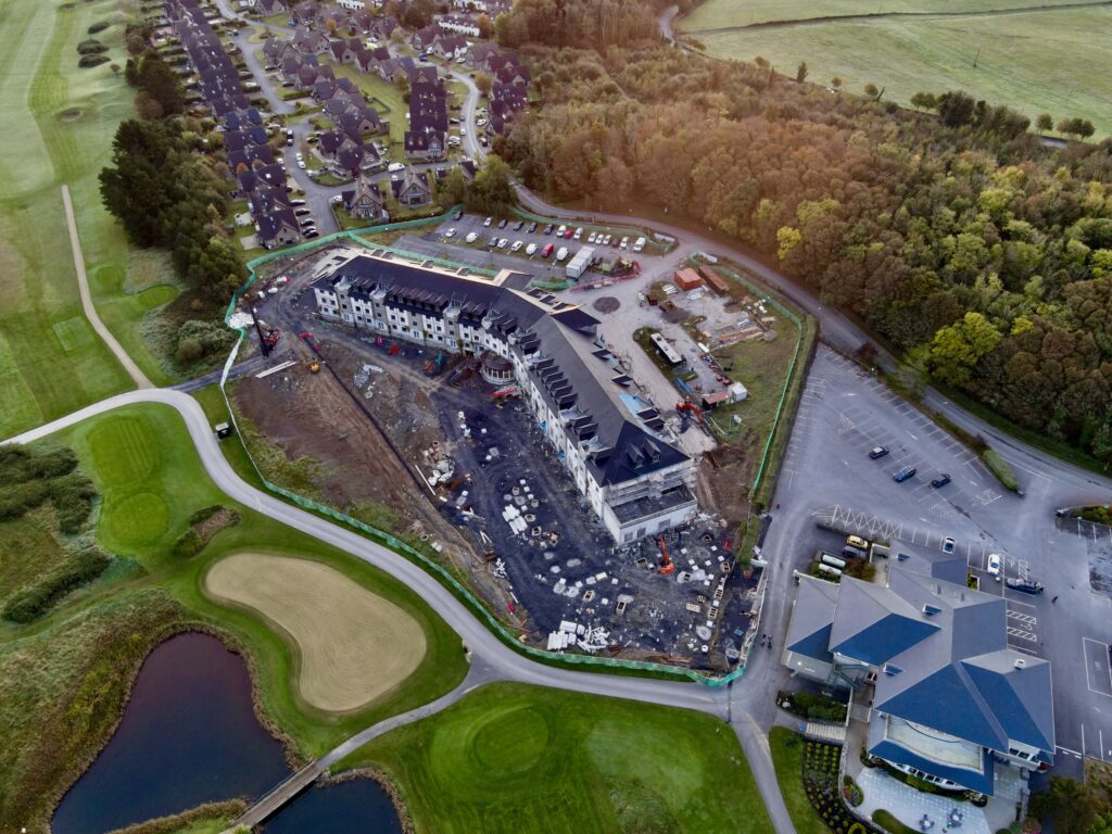 Overhead View of Hotel Development Site – A high-angle aerial view capturing the progress of a hotel construction project, highlighting the surrounding golf course, nearby infrastructure, and the layout of the development site.